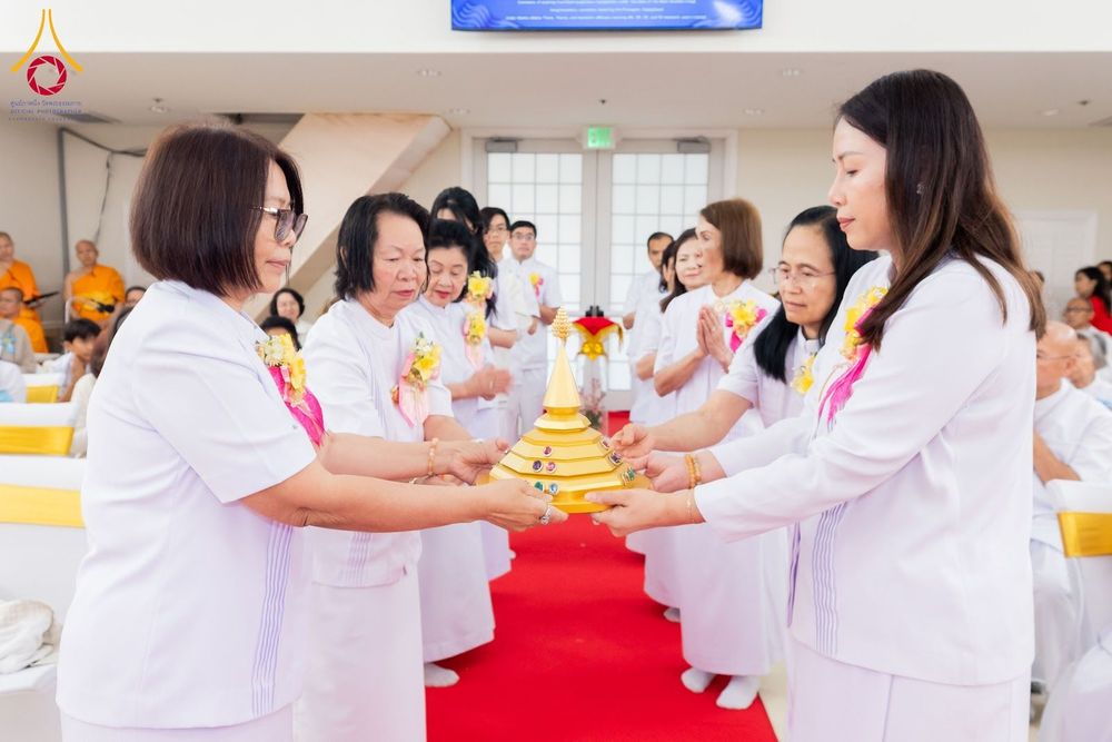 กลุ่มคนสวมชุดขาวกำลังถือพานพุ่มสีทองที่มีพระบรมสารีริกธาตุในพิธีทางศาสนา