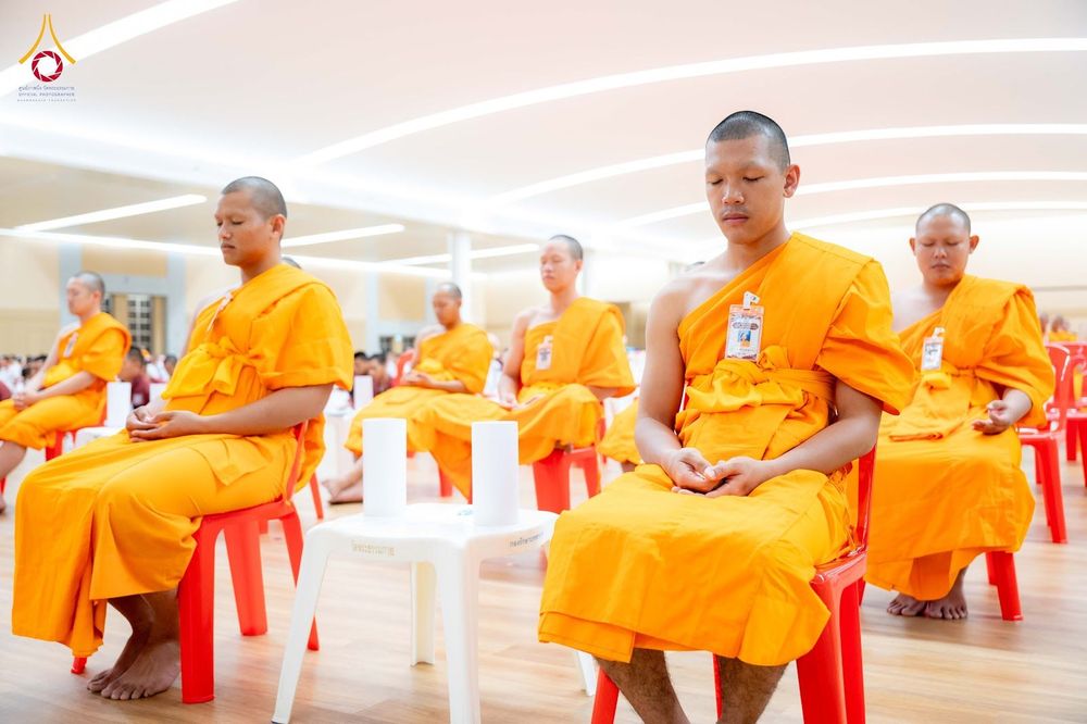 กลุ่มนักเรียนนายสิบตำรวจห่มจีวรนั่งสมาธิเรียงแถวกันภายในห้องโถงกว้าง