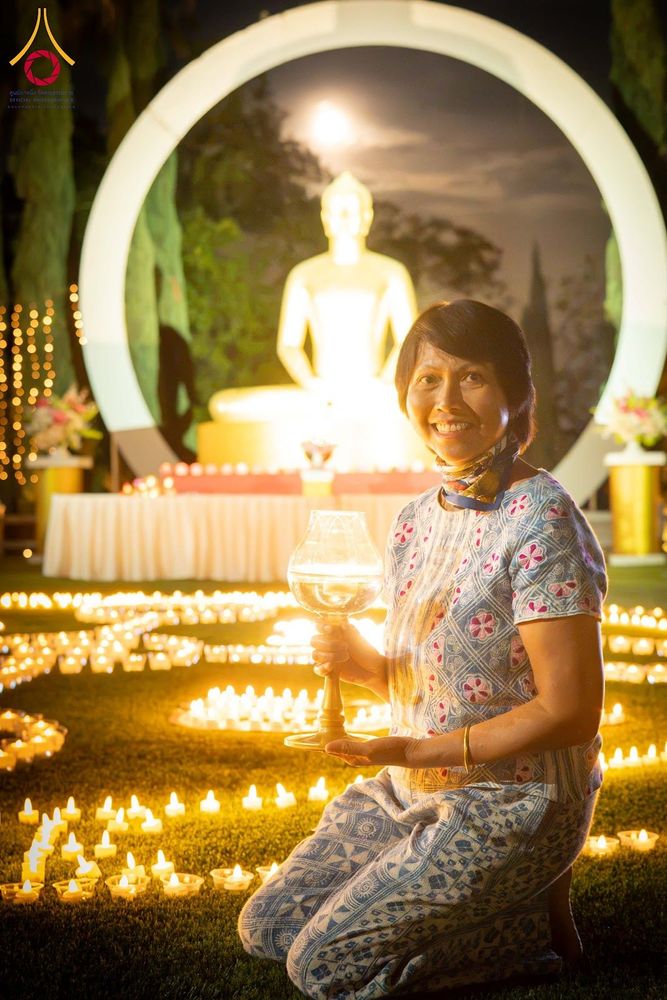 หญิงไทยถือโคมประทีปนั่งอยู่ท่ามกลางแสงไฟจากประทีปจำนวนมากในกิจกรรมจุดประทีปยามค่ำคืน