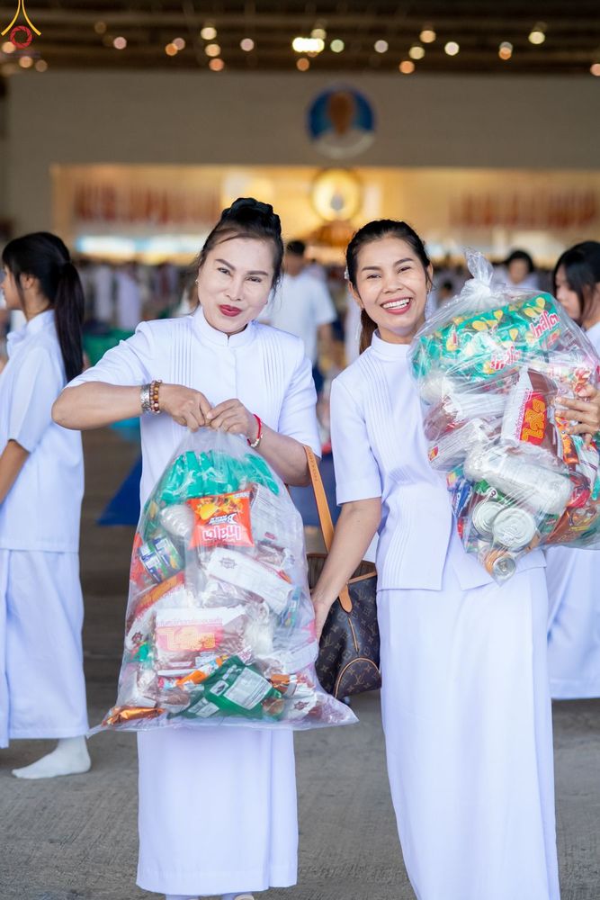 หญิงไทยสองคนสวมชุดสีขาวถือถุงพลาสติกบรรจุอาหารแห้งเพื่อเตรียมตักบาตร