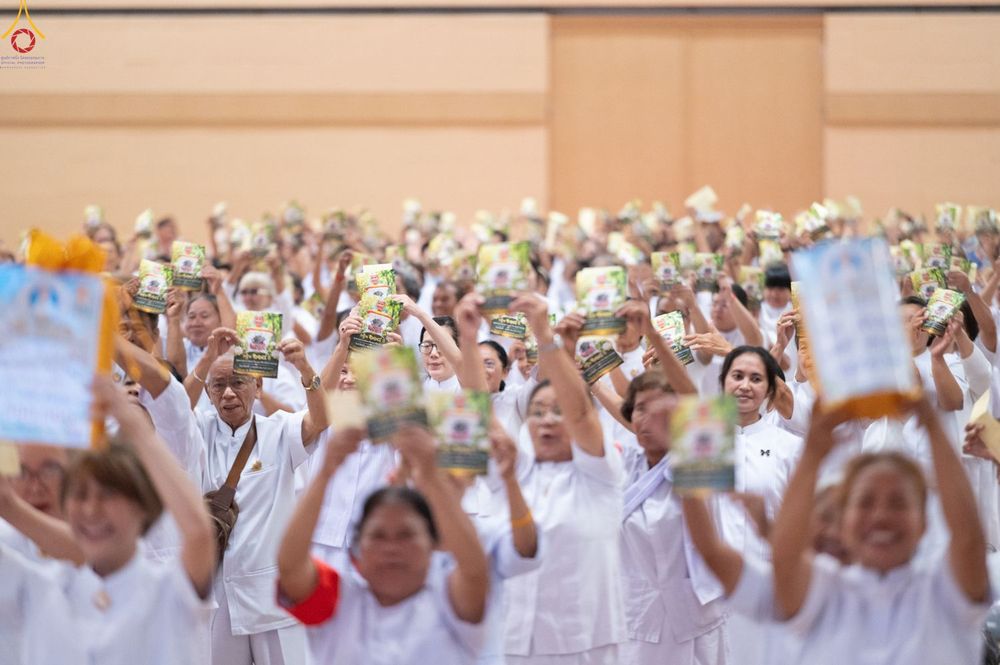 กลุ่มคนสวมชุดสีขาวจำนวนมากกำลังชูแผ่นพับขึ้นเหนือศีรษะในห้องประชุม