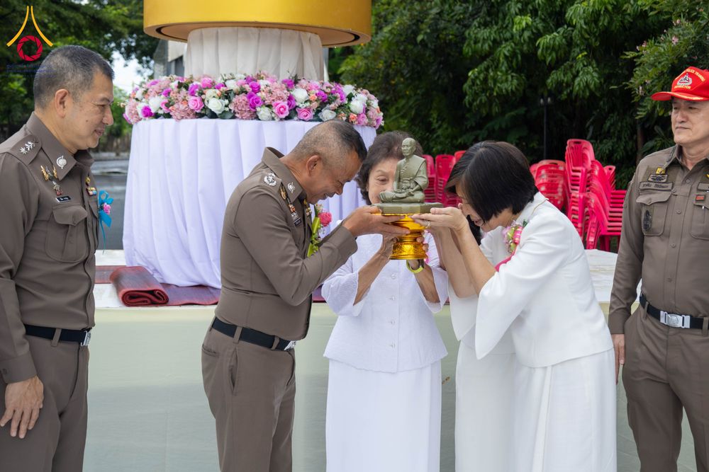 เจ้าหน้าที่ตำรวจและสุภาพสตรีในชุดขาวกำลังประคองพานที่มีพระพุทธรูปขนาดเล็กในพิธีทางศาสนา
