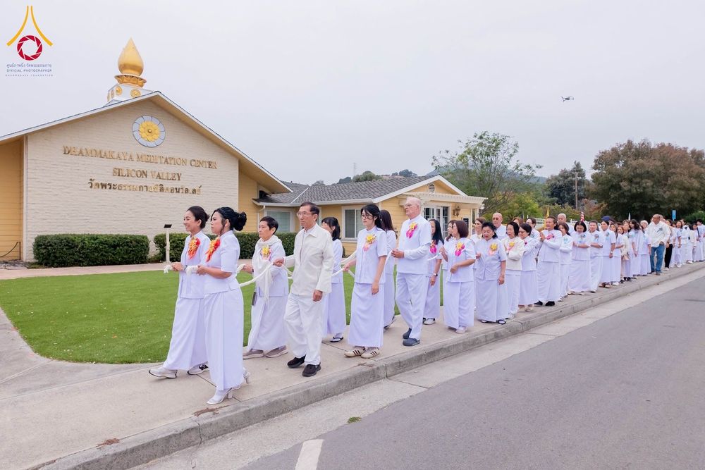 กลุ่มคนสวมชุดขาวเดินแถวถือสายสิญจน์หน้าอาคารวัดพระธรรมกายซิลิคอนวัลเลย์