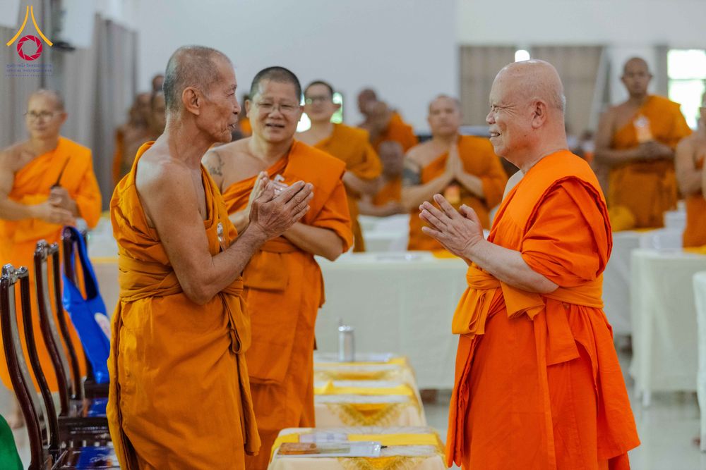 พระสงฆ์หลายรูปในจีวรสีส้มกำลังสนทนาและประนมมือไหว้กันภายในห้องประชุม