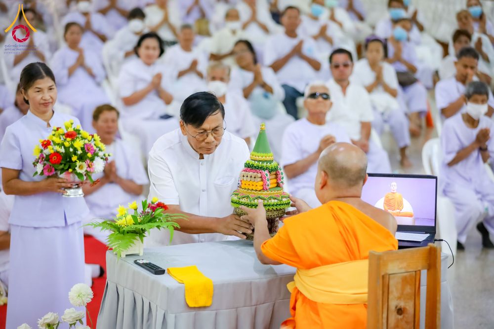 ชายสวมชุดขาวถวายพานพุ่มแด่พระภิกษุสงฆ์ในงานอบรมธรรมะที่มีผู้เข้าร่วมสวมชุดขาวจำนวนมาก