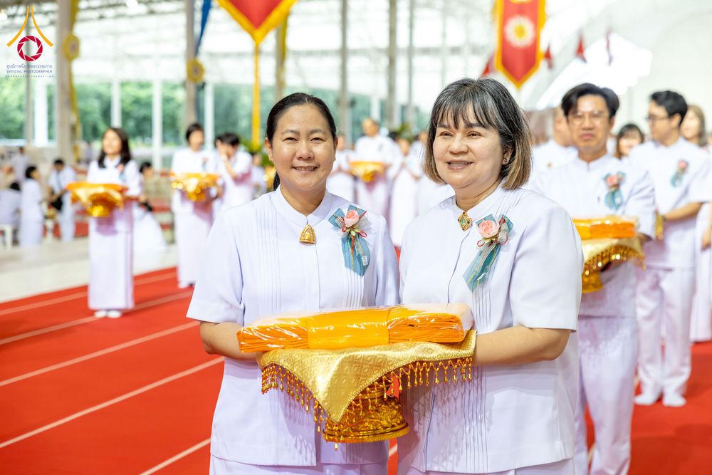 หญิงสองคนสวมชุดสีขาวถือพานผ้าไตรจีวรสีเหลืองทองในพิธีทางศาสนา