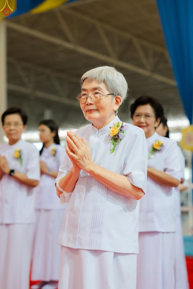 หญิงสูงวัยสวมชุดสีขาวพนมมือด้วยท่าทางสงบในพิธีทางศาสนา
