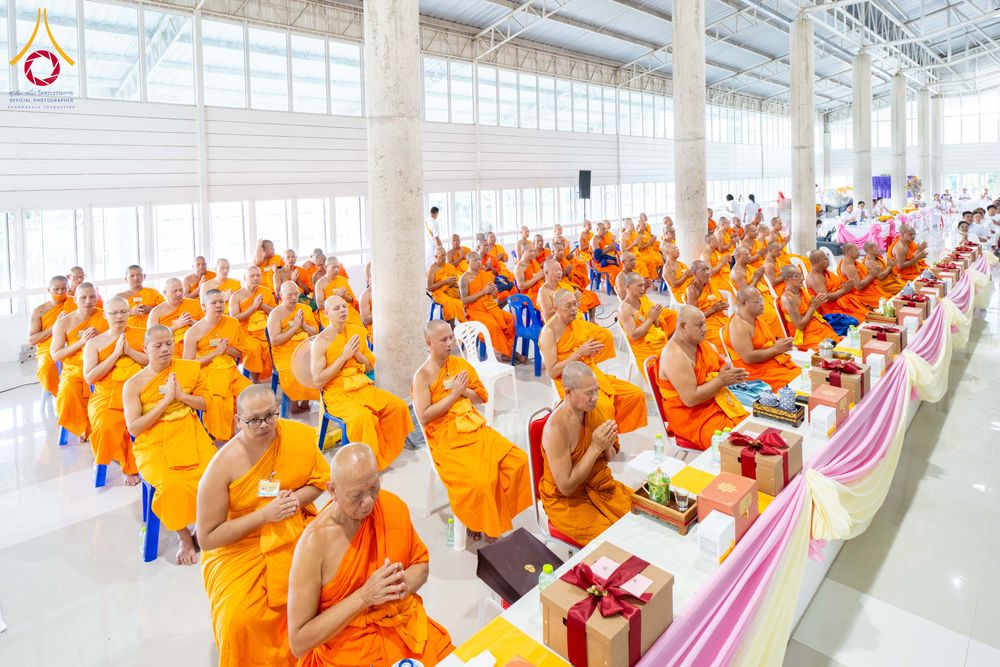 พระภิกษุสงฆ์จำนวนมากนั่งพนมมือร่วมพิธีทางศาสนาภายในอาคารโถงกว้าง