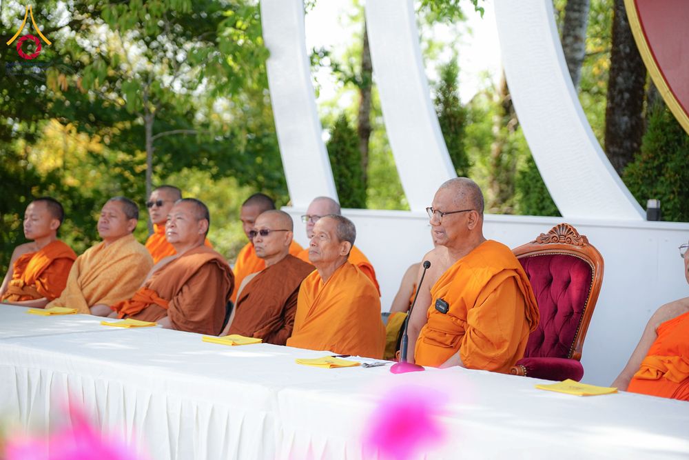 คณะสงฆ์หลายรูปนั่งเรียงแถวบนเก้าอี้หลังโต๊ะยาวในพิธีทางศาสนา