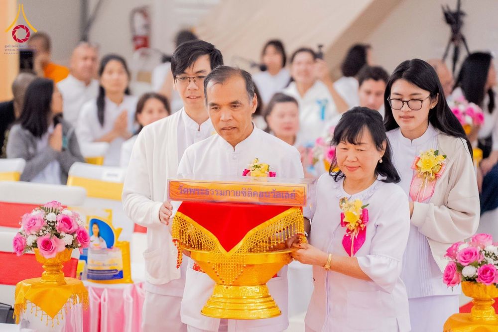กลุ่มคนสวมชุดขาวกำลังถือพานพุ่มที่มีผ้าไตรในพิธีทอดผ้าป่า