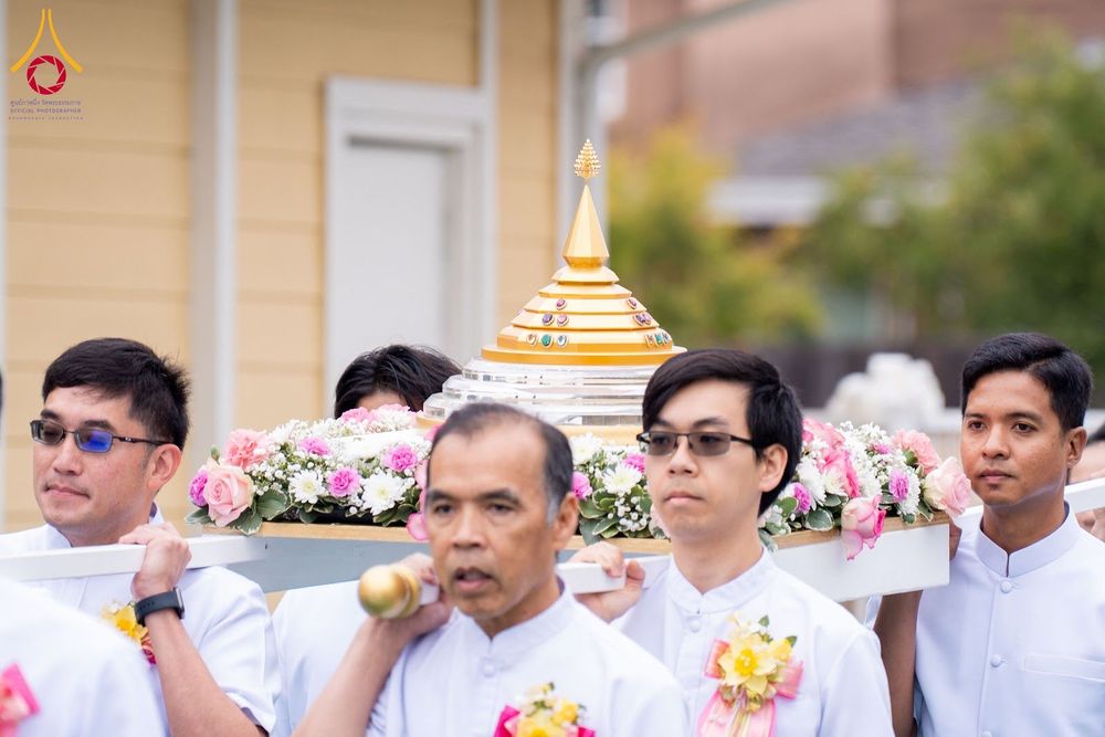 กลุ่มชายสวมชุดสีขาวกำลังช่วยกันแบกเสลี่ยงที่ประดิษฐานพระบรมสารีริกธาตุสีทองตกแต่งด้วยดอกไม้