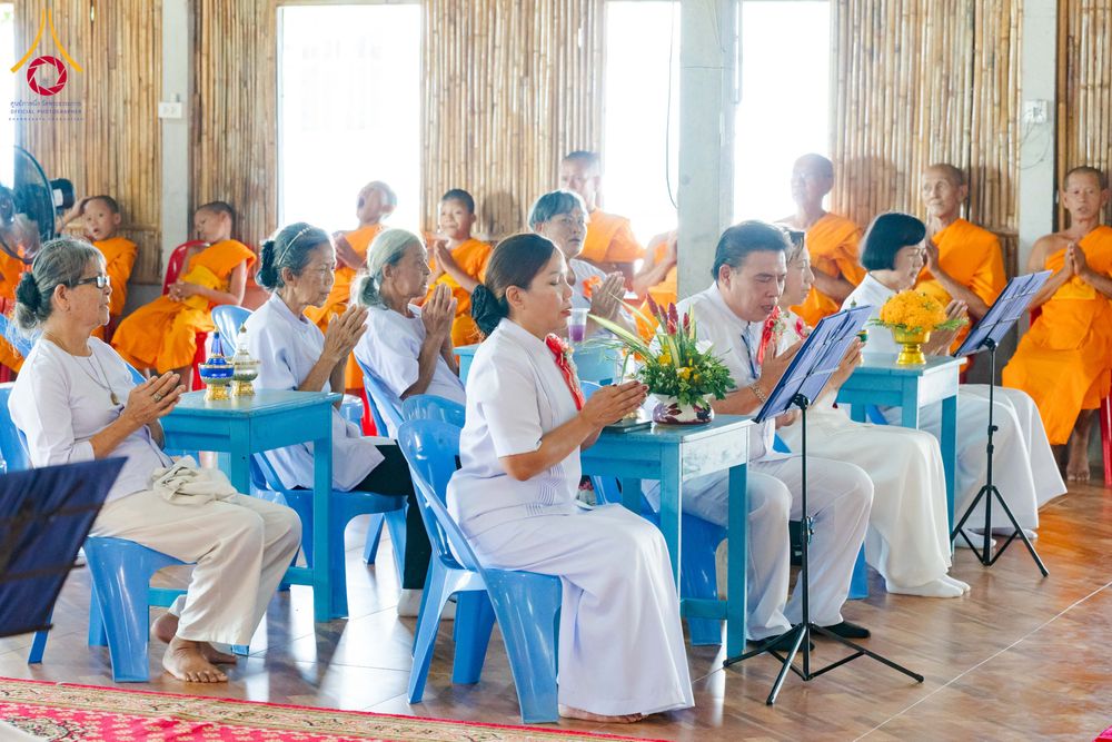 กลุ่มพุทธศาสนิกชนสวมชุดขาวนั่งพนมมือประกอบพิธีทางศาสนาภายในอาคาร