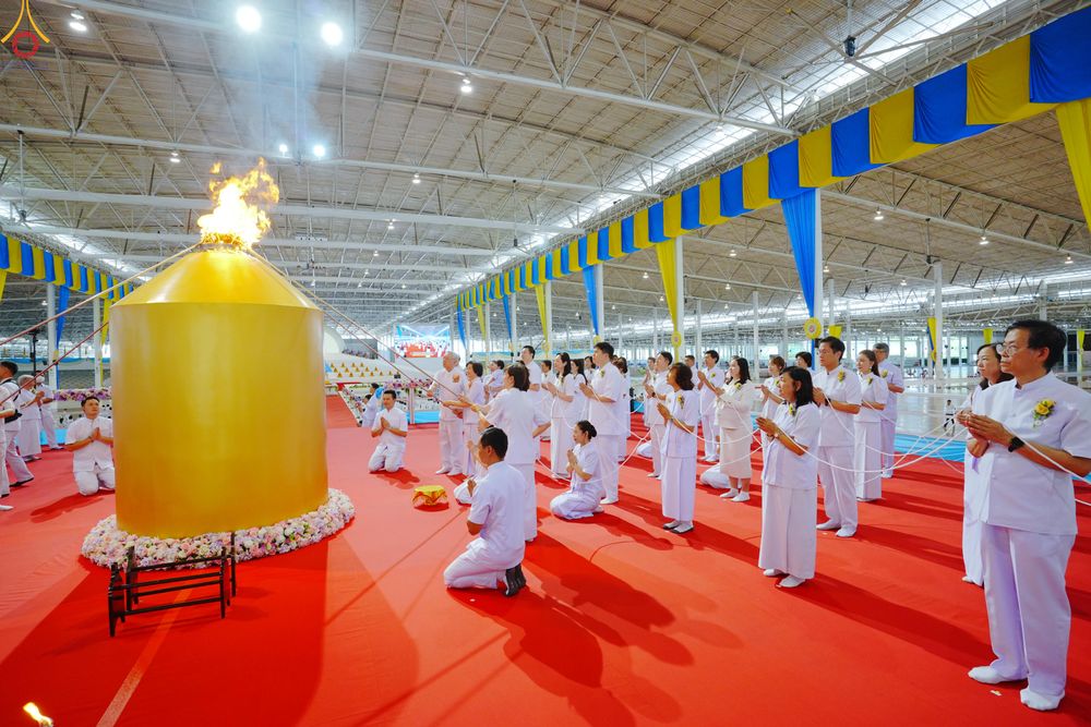 กลุ่มคนในชุดขาวกำลังประกอบพิธีจุดเทียนใจ ไฟนิรันดร์ อนันตชัย ภายในอาคารที่มีการตกแต่งด้วยผ้าสีเหลืองและสีฟ้า