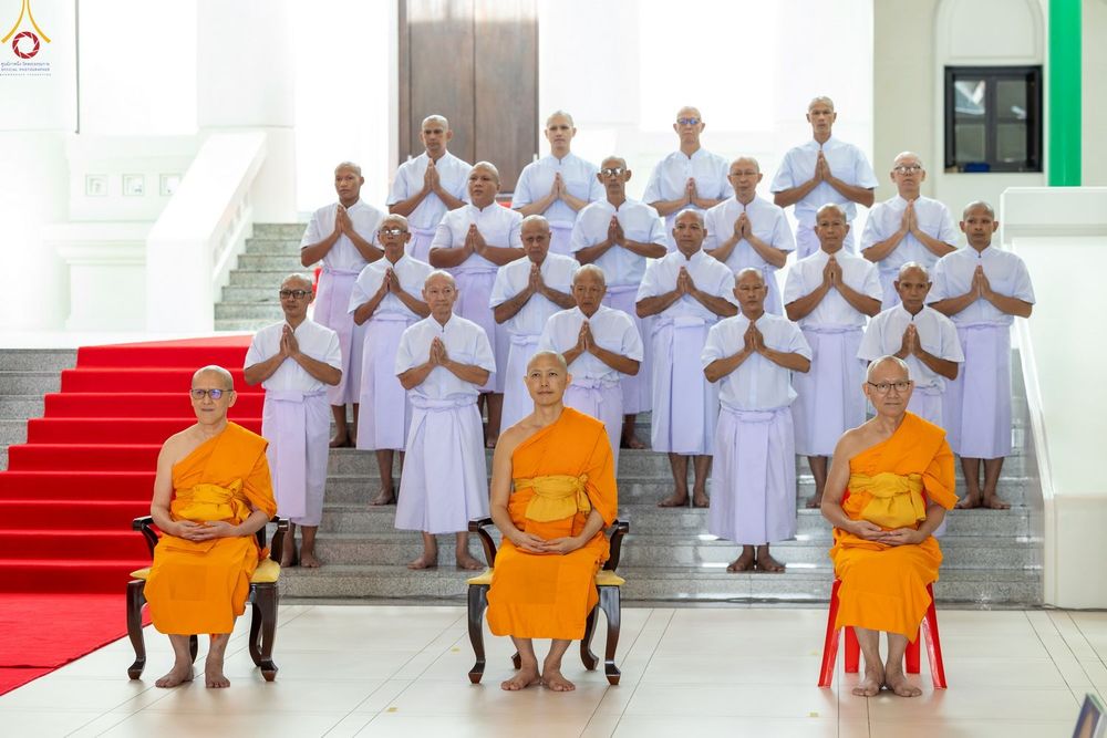 พระภิกษุสงฆ์และนาคในชุดขาวนั่งและยืนเรียงแถวเพื่อถ่ายภาพหมู่ในพิธีอุปสมบท