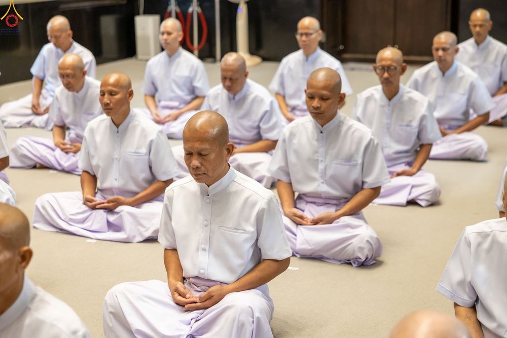 กลุ่มชายสวมชุดสีขาวนั่งขัดสมาธิหลับตาปฏิบัติธรรมภายในอาคาร