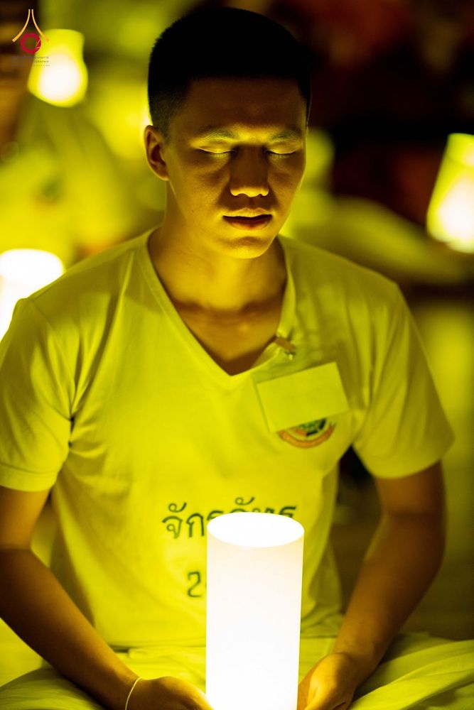 ชายหนุ่มสวมเสื้อสีขาวนั่งหลับตาทำสมาธิและถือโคมไฟส่องสว่างในมือ