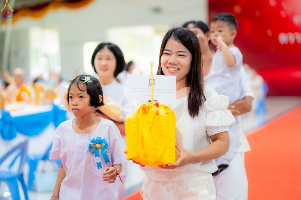หญิงสาวถือถุงสังฆทานสีเหลืองเดินในงานบุญพร้อมกับเด็กๆ