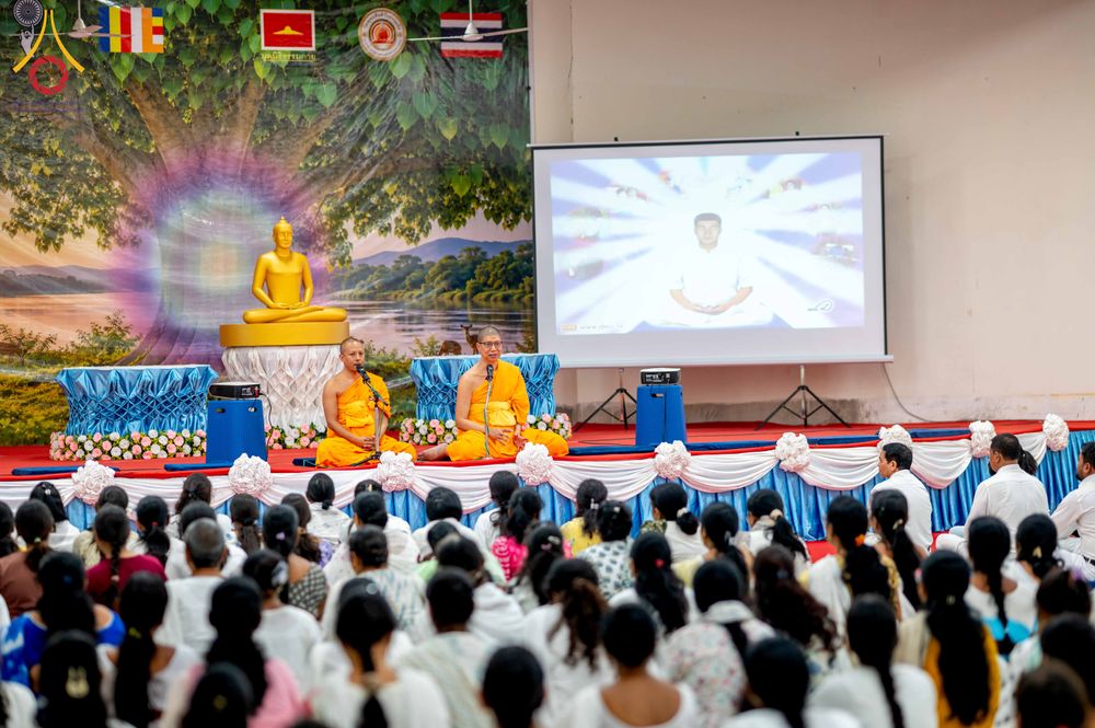 พระภิกษุสงฆ์กำลังบรรยายธรรมบนเวทีต่อหน้าผู้เข้าร่วมโครงการจำนวนมากในห้องประชุม