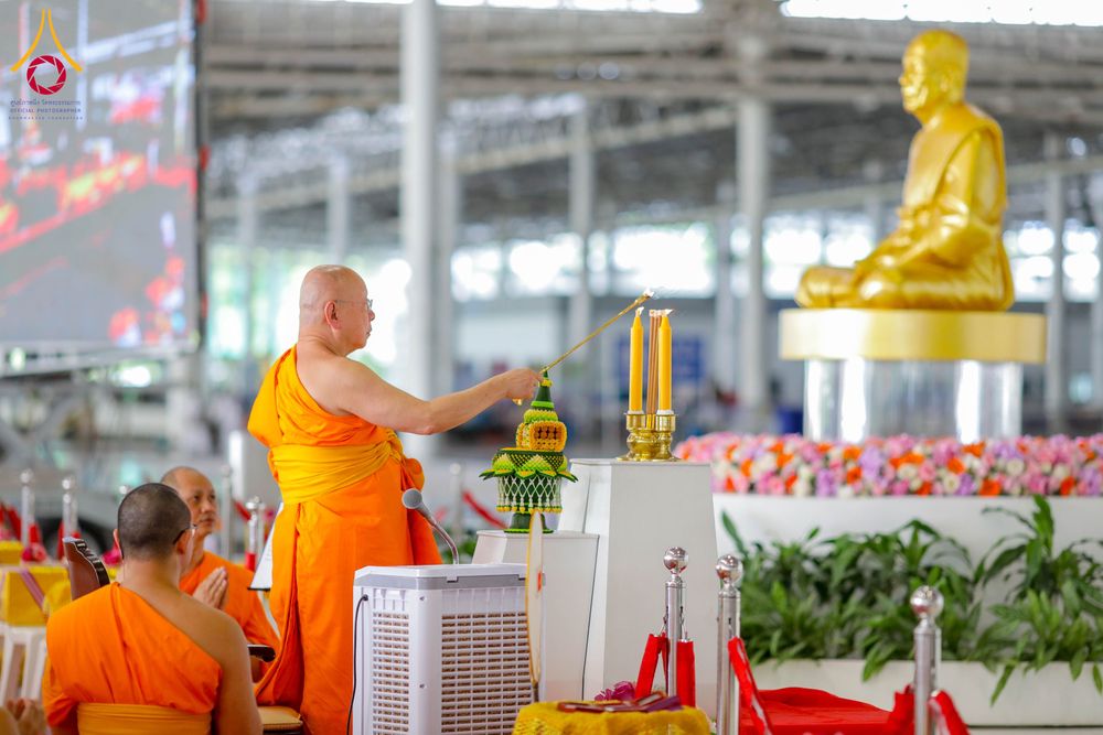 พระภิกษุสงฆ์ในจีวรสีส้มกำลังจุดเทียนบูชาหน้าพระพุทธรูปทองคำในอาคารขนาดใหญ่