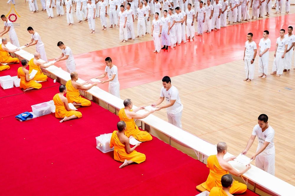 นักเรียนนายสิบตำรวจสวมชุดขาวเข้าแถวรับมอบของจากพระสงฆ์ที่นั่งบนพรมแดงในพิธีปิดโครงการบรรพชา