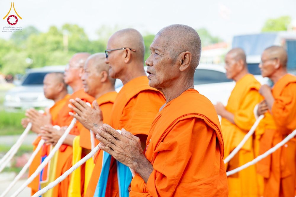 พระภิกษุสงฆ์หลายรูปยืนพนมมือถือสายสิญจน์ในพิธีทางศาสนา