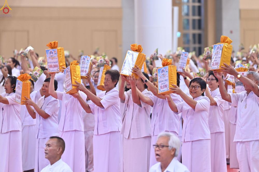 กลุ่มพุทธศาสนิกชนสวมชุดขาวกำลังชูห่อของขวัญสีทองเหนือศีรษะในพิธีทางศาสนา