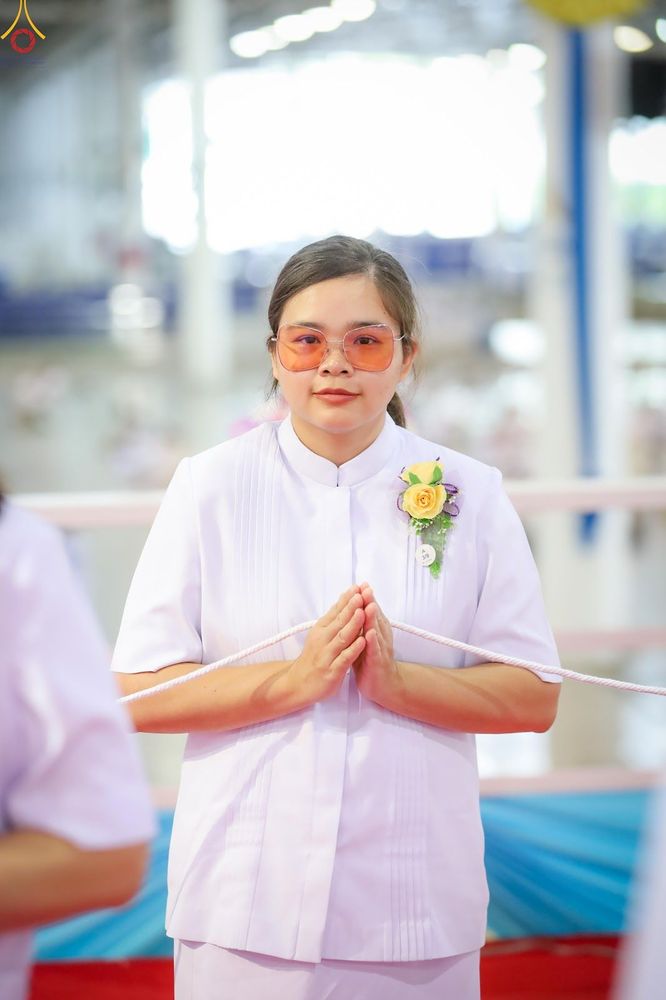 หญิงสาวสวมชุดสีขาวติดดอกไม้ประดับที่หน้าอก กำลังพนมมืออย่างสงบ