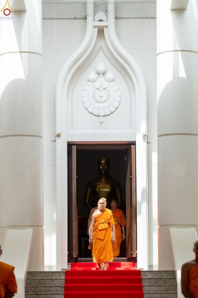พระภิกษุสงฆ์เดินออกจากประตูโบสถ์ที่มีพรมสีแดงปูทางเดินลงมา