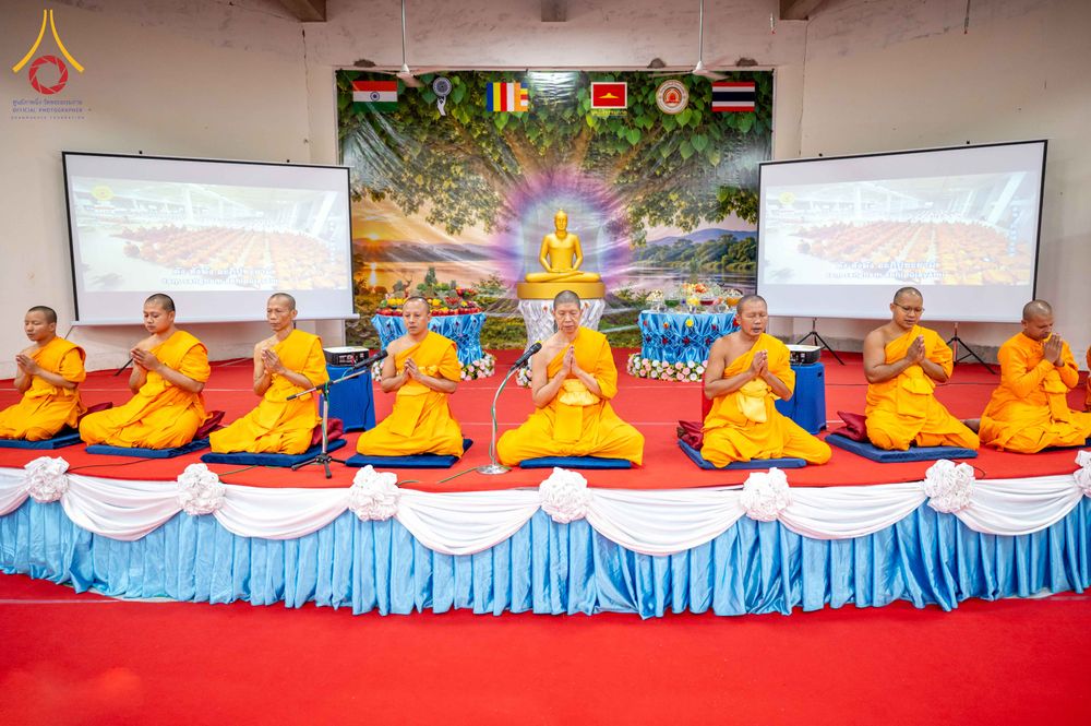 คณะสงฆ์จำนวนหลายรูปนั่งพนมมือเรียงแถวบนเวทีที่มีฉากหลังเป็นภาพพระพุทธรูปและธงชาติหลายประเทศ