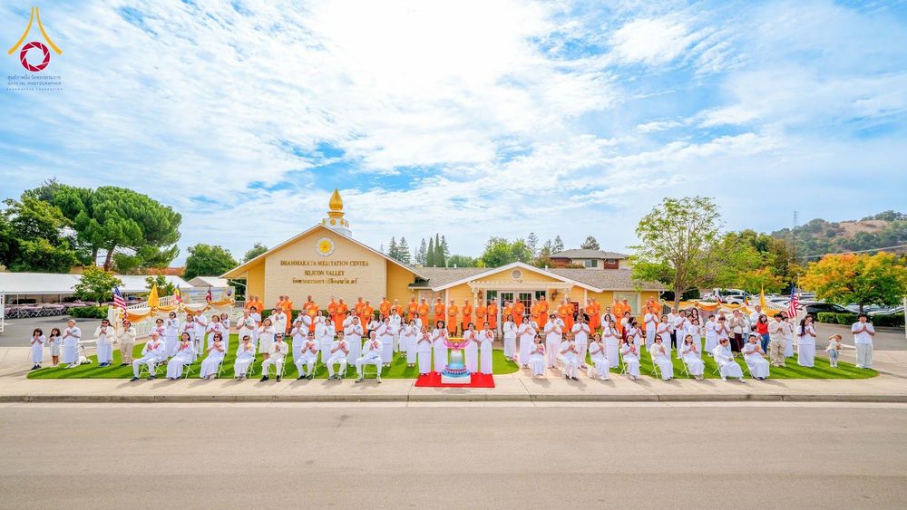 พระภิกษุสงฆ์และสาธุชนชุดขาวจำนวนมากยืนและนั่งเรียงแถวถ่ายภาพหมู่หน้าอาคารวัดพระธรรมกายซิลิคอนวัลเลย์