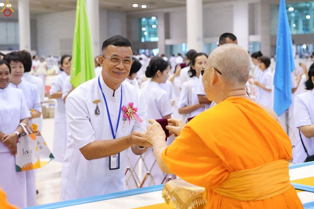 ชายสวมชุดสีขาวกำลังรับมอบพระของขวัญจากพระภิกษุสงฆ์ในพิธี