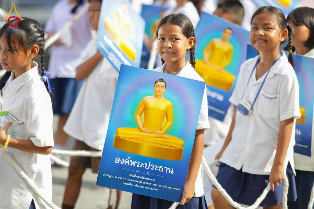 นักเรียนหญิงยิ้มแย้มถือป้ายรูปองค์พระประธานสีทองในกิจกรรมทางศาสนา