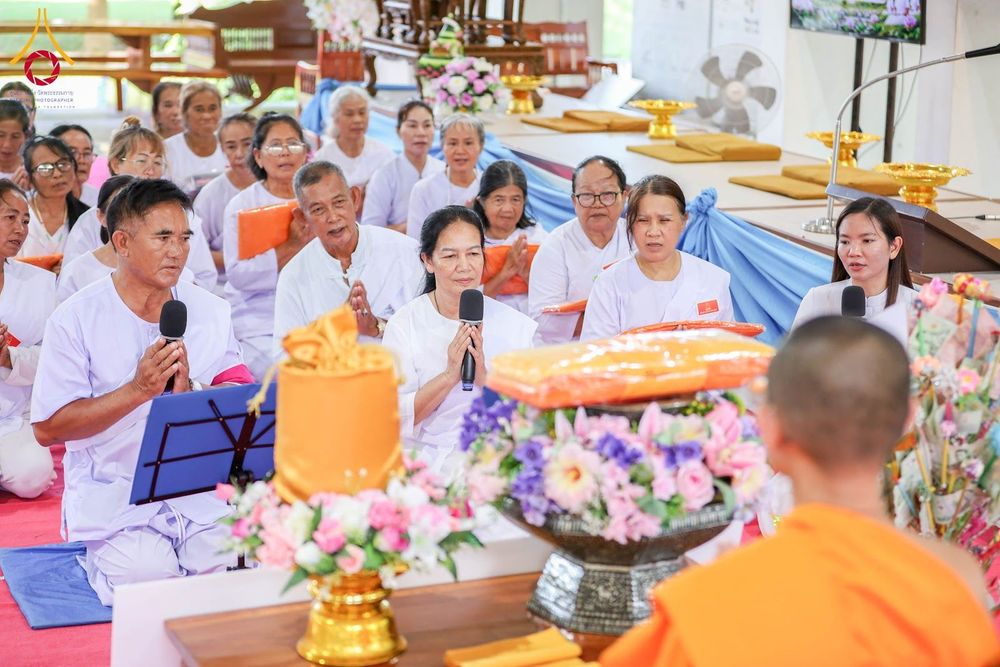 กลุ่มอุบาสกและอุบาสิกาในชุดสีขาวกำลังร่วมกิจกรรมทางศาสนาและถวายสังฆทานภายในอาคาร