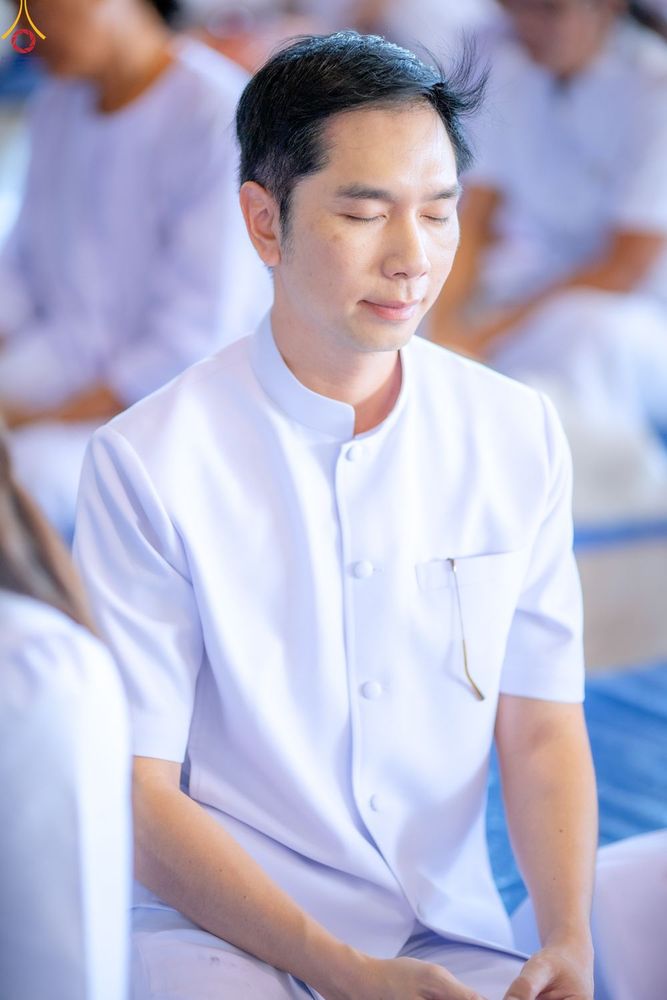 ชายไทยสวมชุดสีขาวนั่งหลับตาทำสมาธิอย่างสงบ