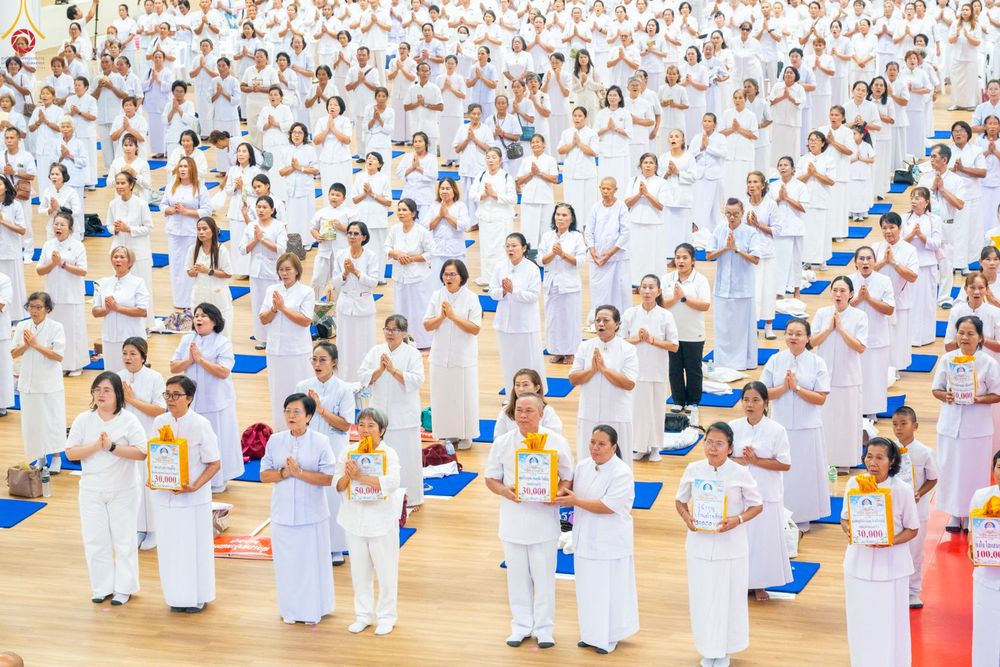 กลุ่มพุทธศาสนิกชนสวมชุดขาวจำนวนมากยืนเรียงแถวร่วมกิจกรรมทางศาสนาภายในอาคาร