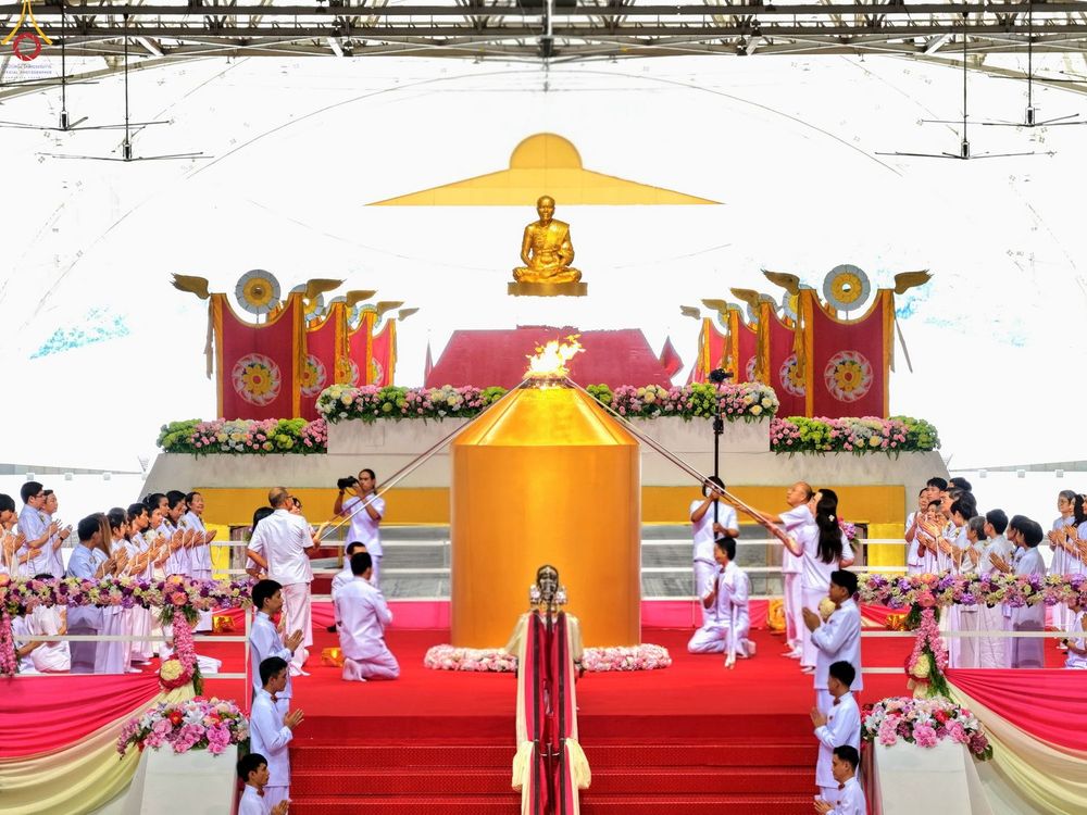 กลุ่มพุทธศาสนิกชนในชุดขาวกำลังประกอบพิธีจุดเทียนใจ ไฟนิรันดร์ อนันตชัย บริเวณหน้าโคมประธานสีทองบนรัตนบัลลังก์