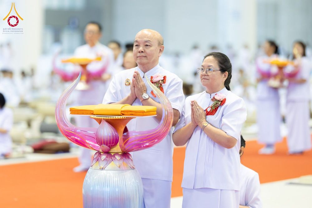 ชายและหญิงสวมชุดสีขาวพนมมือประกอบพิธีทอดผ้าป่า โดยมีพานวางผ้าไตรจีวรอยู่ด้านหน้า