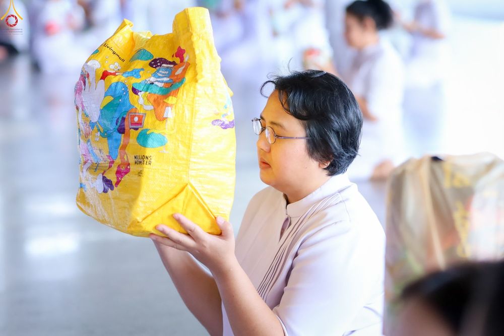 หญิงสวมชุดขาวถือถุงใส่ของทำบุญสีเหลืองในพิธีตักบาตร