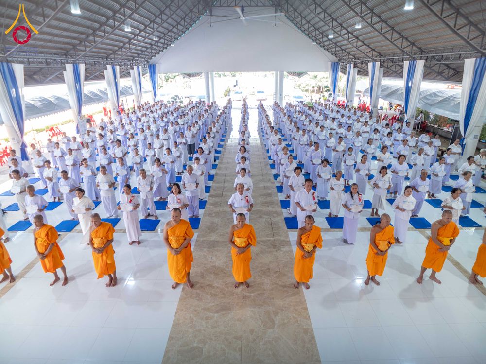 กลุ่มผู้เข้าร่วมโครงการในชุดขาวและพระภิกษุสงฆ์ยืนเรียงแถวภายในอาคารปฏิบัติธรรม