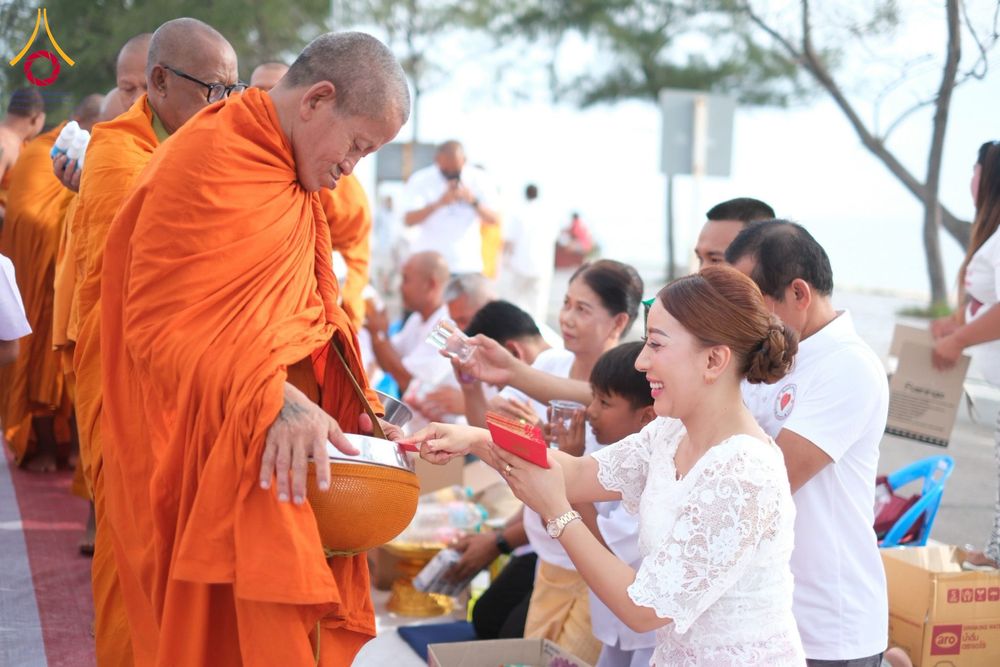 หญิงสาวสวมชุดสีขาวกำลังใส่บาตรพระสงฆ์ในพิธีทำบุญริมชายหาด
