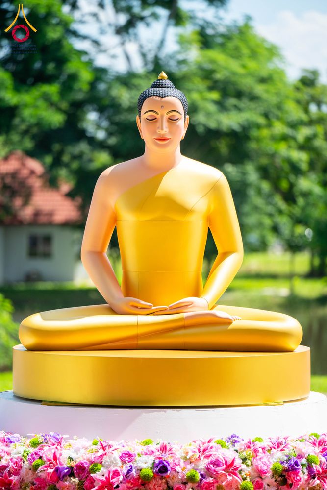พระพุทธรูปปางสมาธิสีทองประทับนั่งบนฐานวงกลม มีดอกไม้ประดับตกแต่งอยู่ด้านหน้า