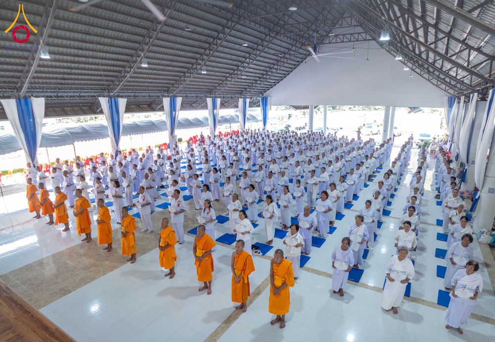 กลุ่มผู้เข้ารับการอบรมในชุดสีขาวและพระภิกษุในชุดสีส้มยืนเรียงแถวภายในอาคารปฏิบัติธรรม