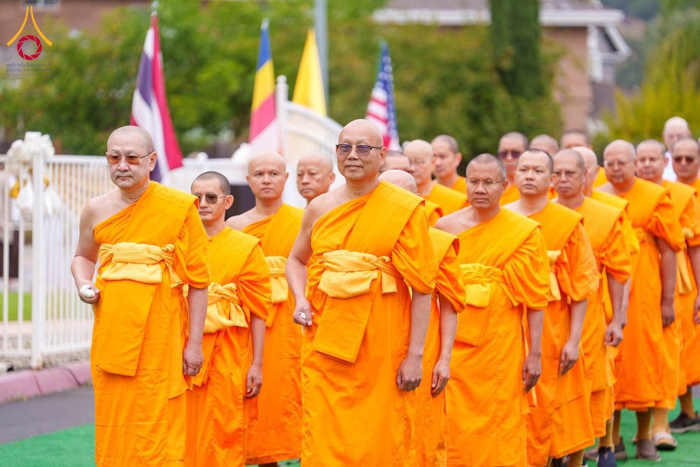 พระภิกษุสงฆ์หลายรูปสวมจีวรสีเหลืองทองเดินแถวในพิธีทางศาสนาท่ามกลางบรรยากาศกลางแจ้ง