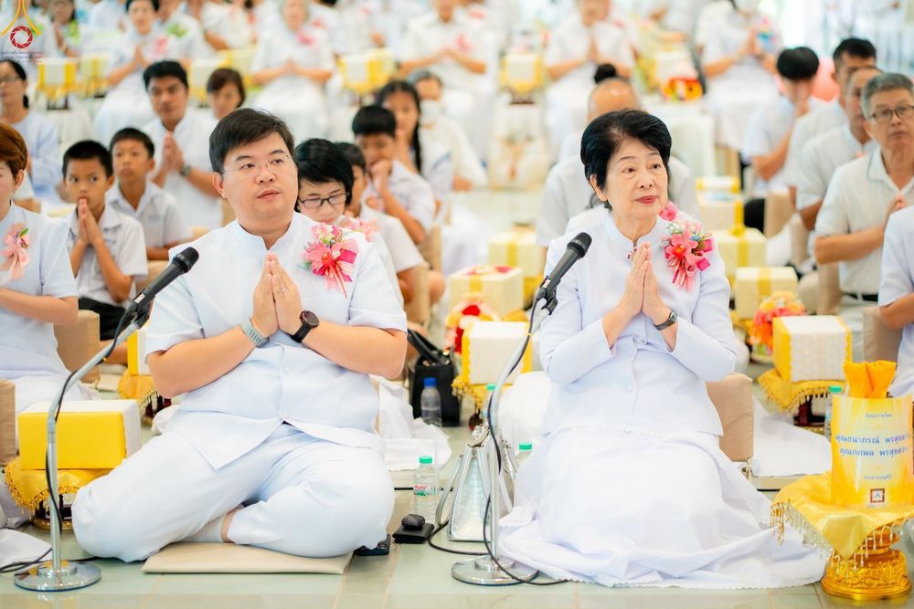 ชายและหญิงสวมชุดสีขาวนั่งพนมมือประกอบพิธีทางศาสนาในงานบุญ