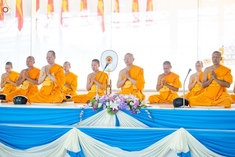 พระสงฆ์หลายรูปนั่งพนมมือบนเวทีที่มีการตกแต่งด้วยผ้าสีฟ้าและสีขาวในพิธีทางศาสนา