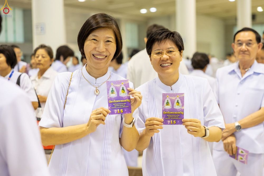หญิงสองคนสวมชุดสีขาวถือบัตรรับพระของขวัญสีม่วงในงานพิธี