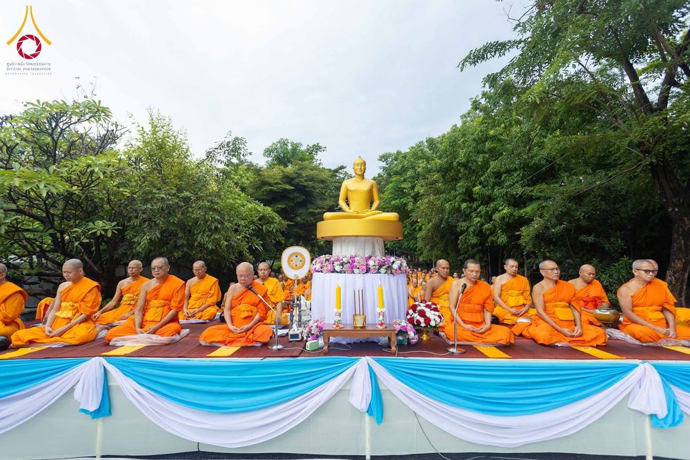 พระสงฆ์หลายรูปนั่งสมาธิบนเวทีที่มีพระพุทธรูปสีทองตั้งอยู่ท่ามกลางสวน