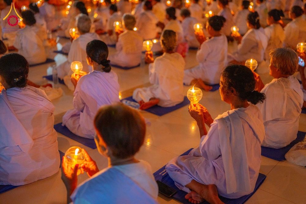 กลุ่มอุบาสิกาในชุดขาวนั่งสมาธิถือประทีปในมือภายในอาคาร