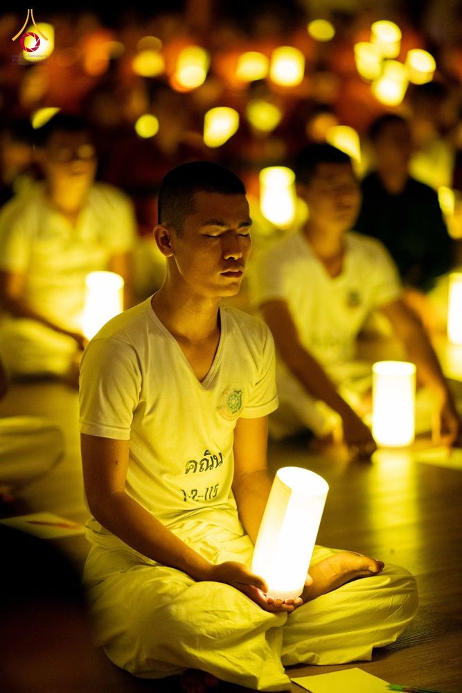 นักเรียนนายสิบตำรวจสวมชุดสีขาวนั่งสมาธิถือเทียนส่องสว่างในบรรยากาศที่มีแสงเทียนโดยรอบ
