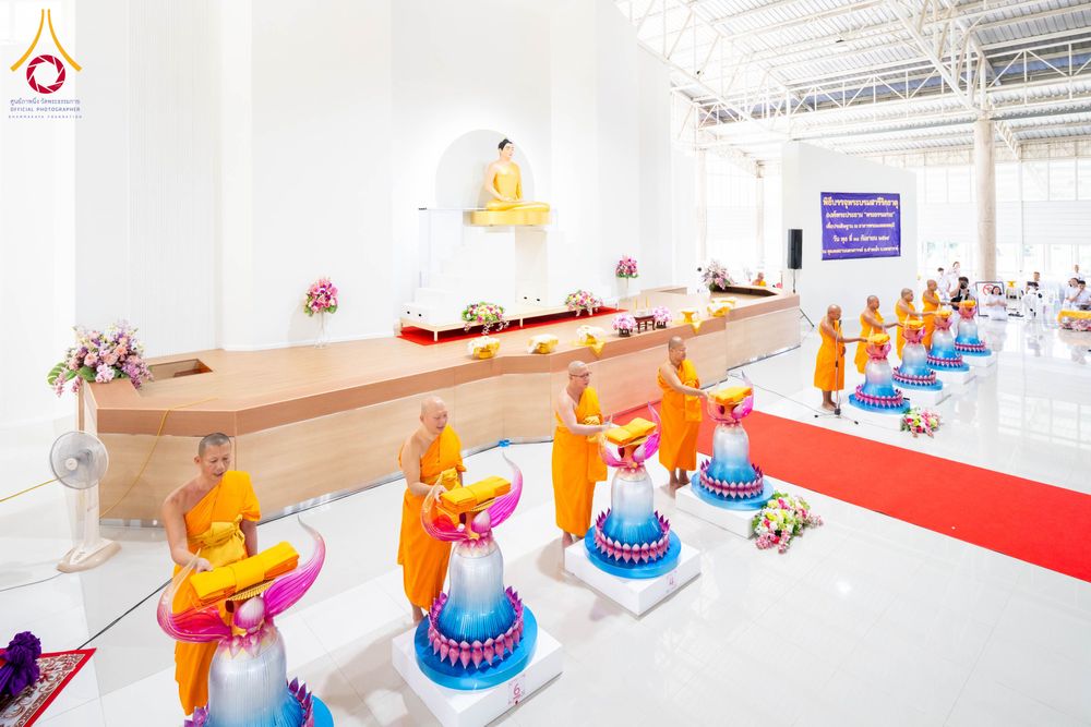 พระภิกษุสงฆ์ในจีวรสีส้มกำลังประกอบพิธีทางศาสนาหน้าเกศดอกบัวตูมจำลองภายในอาคาร